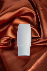 Cosmetic product in tube, bottle, lotion or serum on shiny cloth background