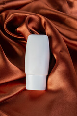 Cosmetic product in tube, bottle, lotion or serum on shiny cloth background