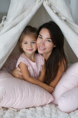 Young mom and little girl surrounded by soft pillows in a teepee. 