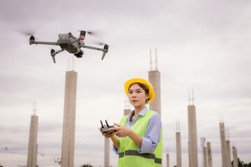 A female construction worker in a safety vest and hard hat operates a drone on-site, using smart technology for surveying, inspection, and monitoring in modern engineering projects.