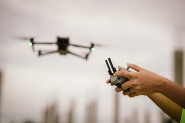 A woman operates a drone using a handheld remote control outdoors, showcasing modern technology,...