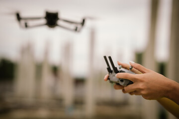 A woman operates a drone using a handheld remote control outdoors, showcasing modern technology,...