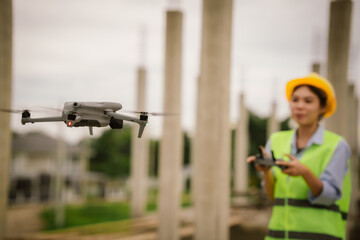 A female construction worker in a safety vest and hard hat operates a drone on-site, using smart technology for surveying, inspection, and monitoring in modern engineering projects.