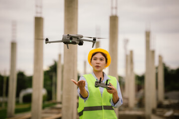 A female construction worker in a safety vest and hard hat operates a drone on-site, using smart technology for surveying, inspection, and monitoring in modern engineering projects.