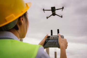A female construction worker in a safety vest and hard hat operates a drone on-site, using smart technology for surveying, inspection, and monitoring in modern engineering projects.