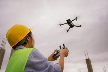 A female construction worker in a safety vest and hard hat operates a drone on-site, using smart technology for surveying, inspection, and monitoring in modern engineering projects.