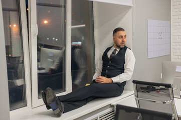 Thoughtful Caucasian man sitting on windowsill in office. 