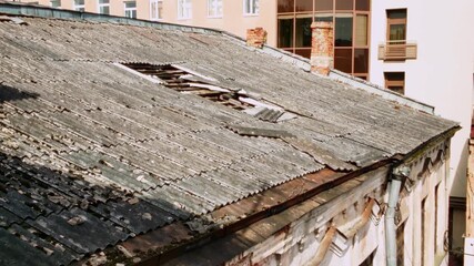 Close-up of a weathered corrugated rooftop with visible structural damage and missing panels. Background shows modern residential buildings. Shot in Daugavpils, Latgale, Latvia - Powered by Adobe