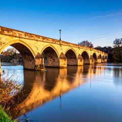 Fototapeta premium Historic stone bridge over calm river at dawn