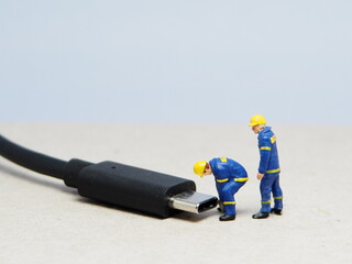 Mini toy of action figure at table with blurred background. Miniature photography concept design. Minifigure of engineer character fixing the USB port device.