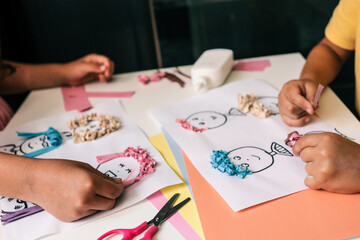 Children’s hands creating paper collage with cartoon faces, using colorful paper and glue....