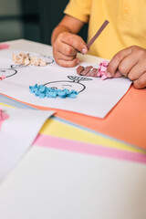 Close-up of a child's art table with colorful pastel paper, pink paper scraps, glue, and a handmade...