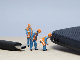 Mini toy of action figure at table with blurred background. Miniature photography concept design. Minifigure of engineer character fixing the USB port device.