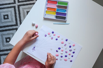 Child making a colorful balloon artwork from clay dots on paper. Purple, pink, and white modeling...