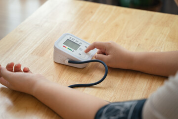 An Asian woman uses a portable blood pressure monitor in her living room. Health awareness concept.