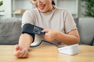 An Asian woman uses a portable blood pressure monitor in her living room. Health awareness concept.