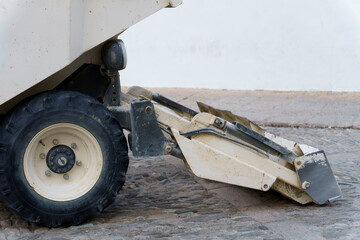 Close-up of a dumper truck lowering its shovel on a cobblestone street during road construction or...