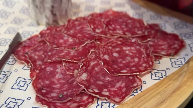 Thin slices of saucisson salami displayed on decorative paper showing marbled texture
