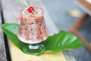 A glass of iced chocolate drink topped with a red cherry on a skewer