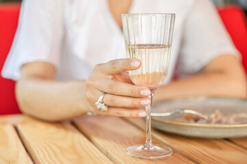 Cheerful woman in summer cafe enjoying ravioli and sparkling wine. Girl sitting on terrace, holding her belly after eating, happy and relaxed in warm weather.
