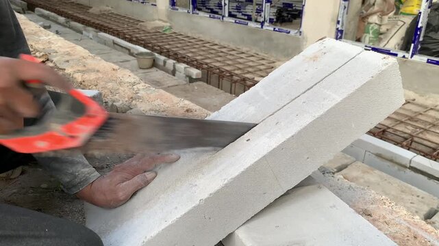 Hands of construction worker or handyman is cutting lightweight bricks or hebel using a saw. The process of breaking lightweight bricks that will be used to make the walls of a building