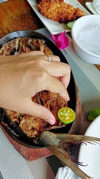 Overhead handheld motion showing a hand squeezing calamansi over fried marinated bangus or milkfish, authentic local traditional Filipino dish from the Philippines