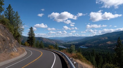 Fototapeta premium Scenic Highway Curving Through Mountain Landscape Under Bright Blue Sky with Fluffy White Clouds