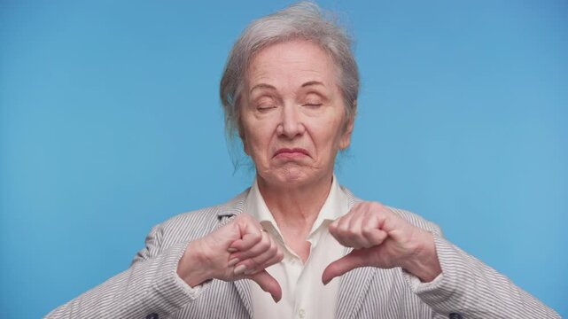 Displeased senior woman showing thumbs down gesture on blue