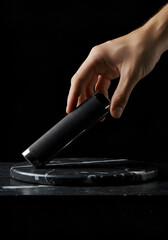 Hand holding a black cylinder on a dark marble disc