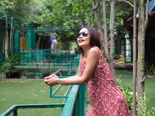 Stylish Asian woman in floral dress leaning on a green railing in a colorful outdoor setting