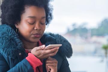 Young woman in winter clothes sending a message or audio with mobile phone in the park