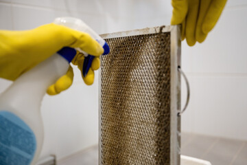 Cleaning dirty kitchen range hood grease filter with spray bottle and rubber gloves