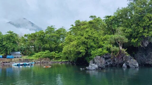 The striking basalt outcrop known as Black Rock, located on Ternate Islands, surrounded by clear turquoise tropical ocean and reef.