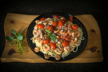 ready to eat and served on a black plate - noodles with shrimp, cherry tomatoes and fresh herbs out the garden