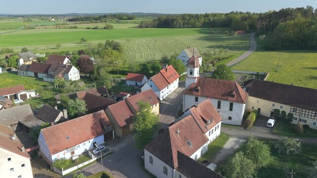 A drone fly over during Spring across a small Franconia village called Thann nearby Ansbach embedded in green landscape and and a small river
