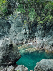 Air Biru Faudu is a hidden gem destination on Hiri Island, North Mollucas, Indonesia that offers views of crystal clear blue water amidst lush trees and black rocks. © Novi