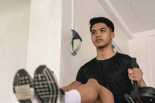 A young handsome asian man does a set of captain's chair leg raises at the gym. Training and strengthening abs.