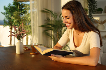 Happy woman at sunset reading paper book in a house