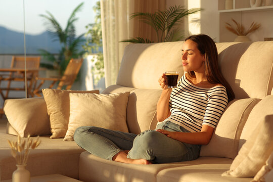 Woman smelling coffee aroma relaxing at sunset at home