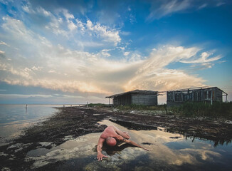 Nude figure in water, cloudy sky, rustic shore, black and white.