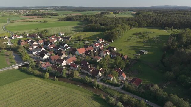 A drone fly over during Spring across a small Franconia village called Thann nearby Ansbach embedded in green landscape and and a small river