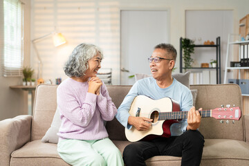Senior couple with guitar for music and singing together on sofa for retirement lifestyle . Happy elderly woman or creative musician people in living room home playing love song.