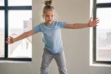 Child practicing a dance routine in a bright room with large windows and city view