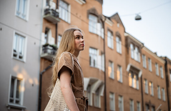 Young woman with mesh bag walking on city street in summer evening