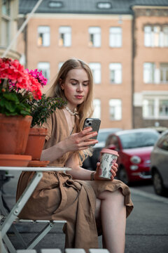 Young woman drinking coffee at outdoor cafe and using smartphone