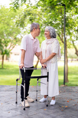 Happy loving Asian senior couple taking a walk with walker in the park.