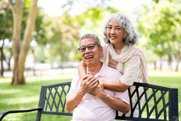 Senior couple, hugging and sitting at bench outdoor in a park with love, care and support in...