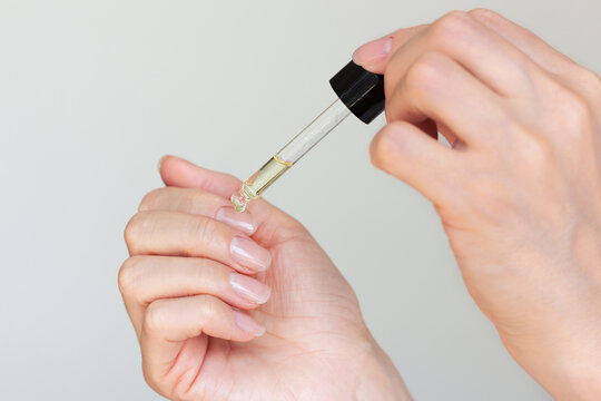 Young woman with a beautiful manicure applying a drop of oil with a pipette to the cuticle around the nails to moisturize.