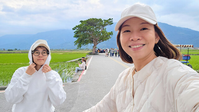 A young lesbian couple smiling cycling through Mr. Brown Avenue in Chishang, Taitung, Taiwan &mdash; romantic self-guided journey through rice paddies and countryside, backpacking travel selfie