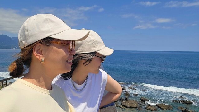 A young lesbian couple on a romantic self-guided road trip along the coastal blue beach in Taitung, Taiwan — joyful summer backpacking journey, road Travel
